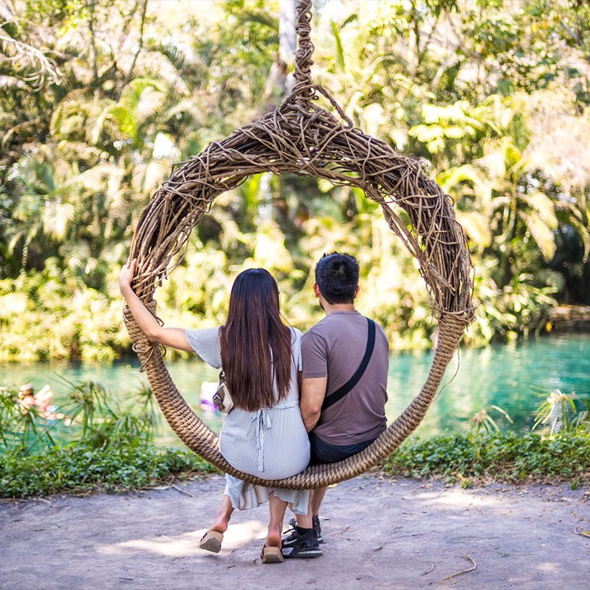 Una pareja sentada en un columpio de ramas frente al río