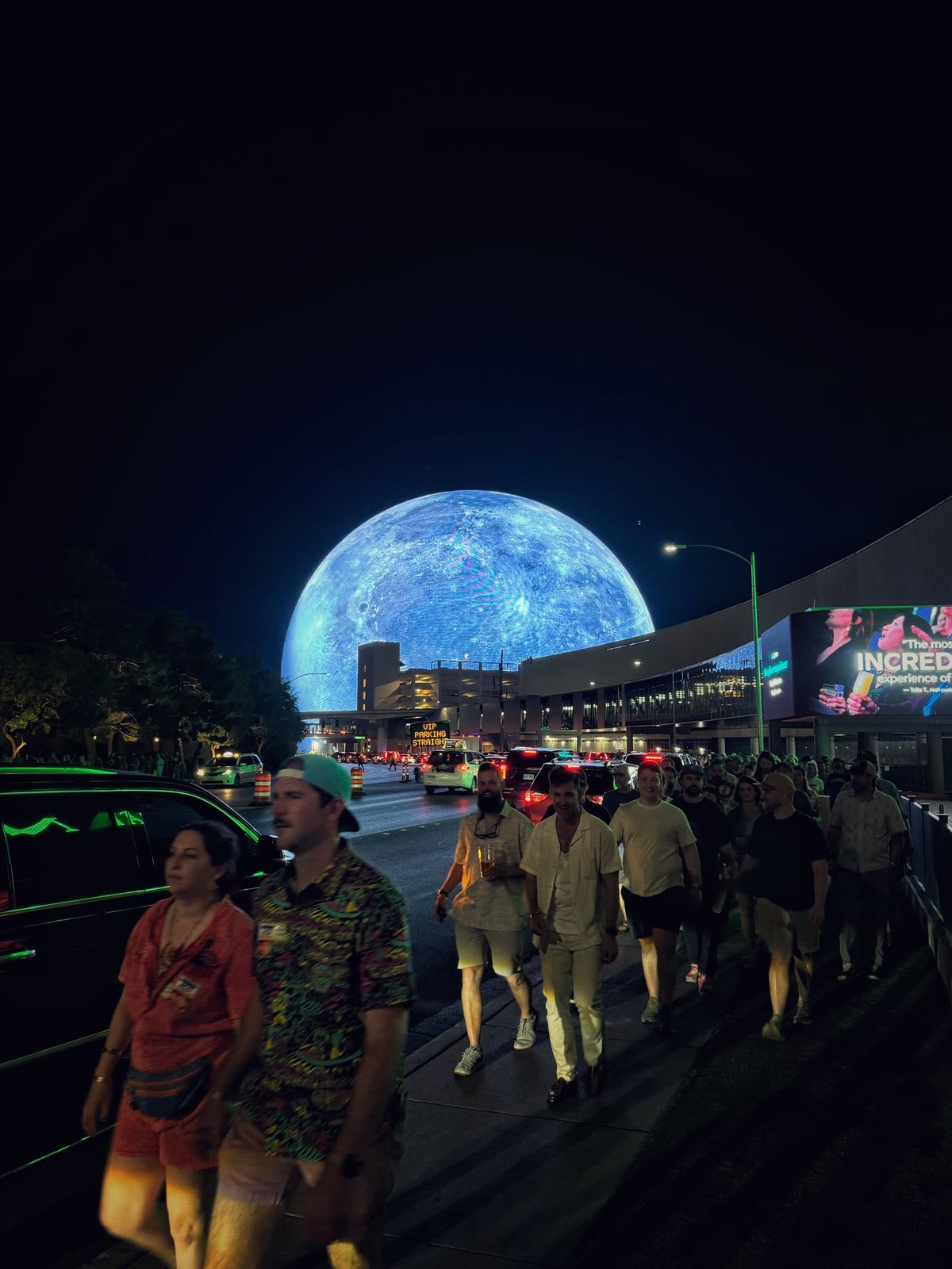 Gente que camina de noche frente a Sphere, que brilla como una luna