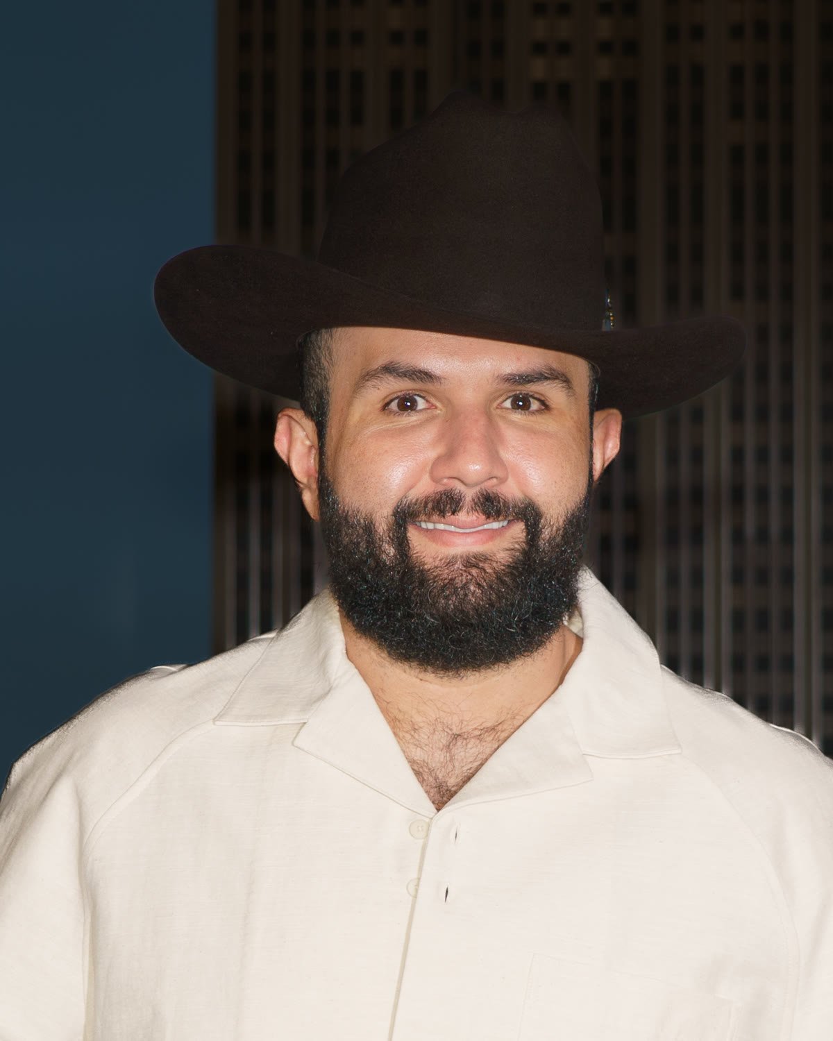 Carín León con sombrero y camisa clara, sonriendo
