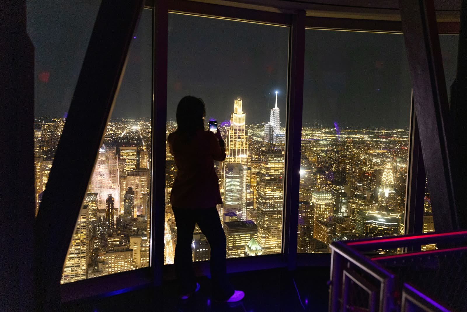 Una persona fotografía la ciudad iluminada desde el piso 102