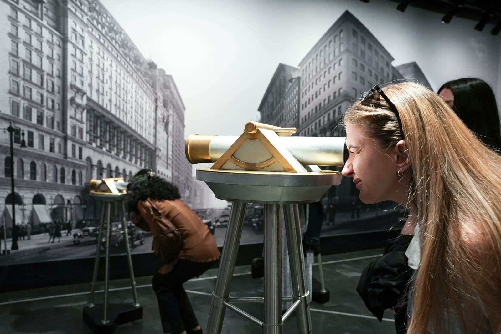 Dos personas se asoman por visores de topógrafo frente a una foto antigua de Nueva York
