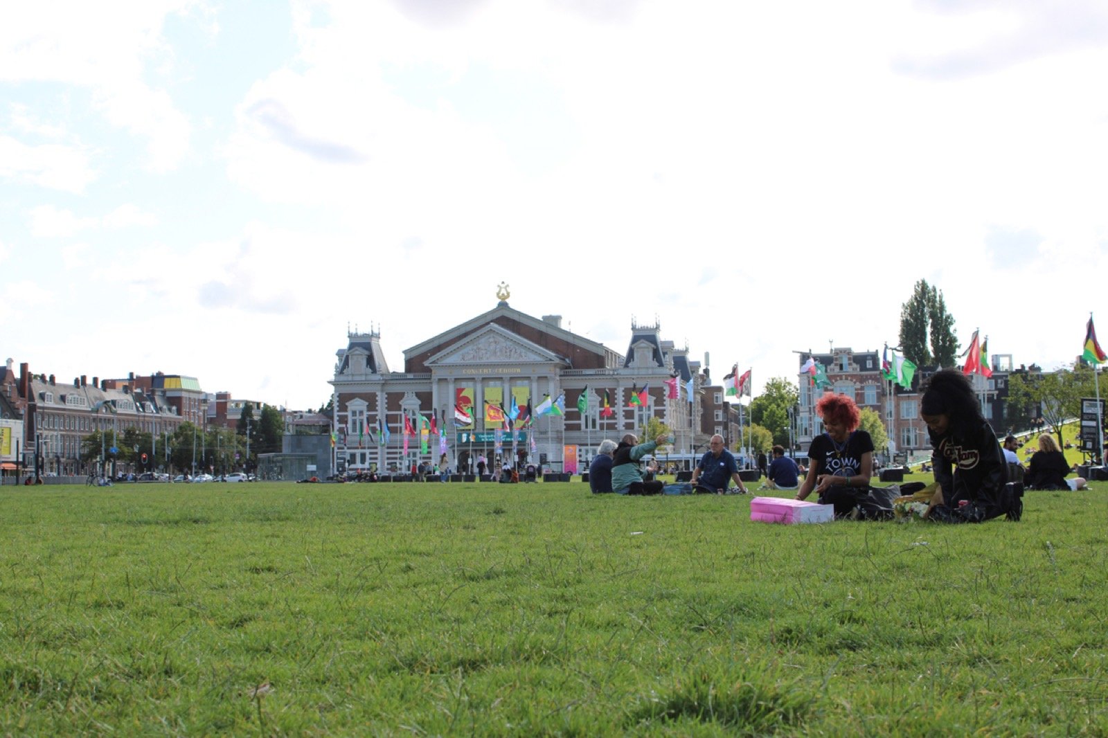 Gente en el pasto del Museumplein, con el Concertgebouw al fondo