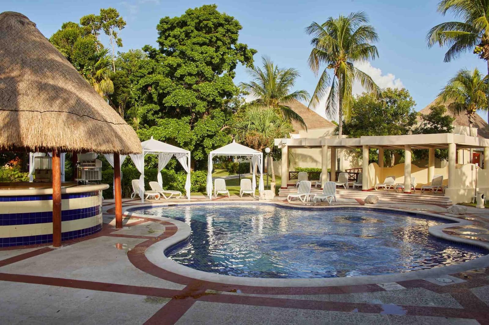 Alberca con jacuzzi, camastros y camas balinesas bajo palmeras