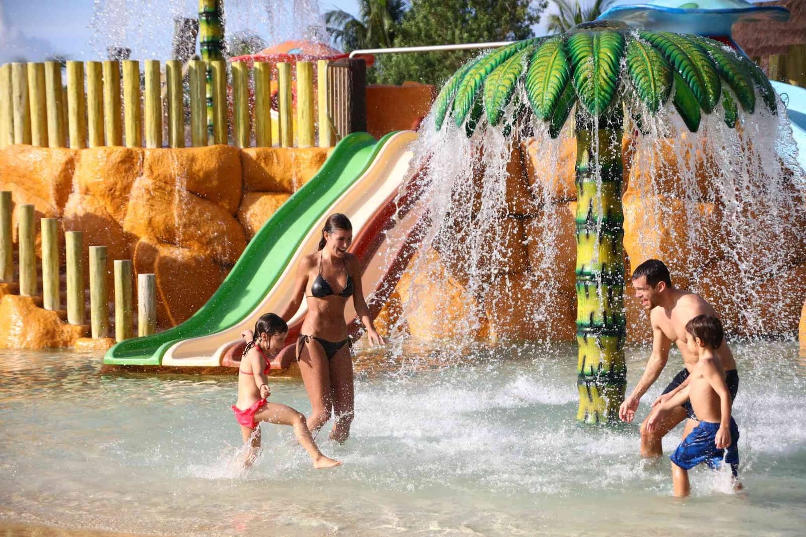 Niños jugando bajo una cascada en forma de palmera en el chapoteadero