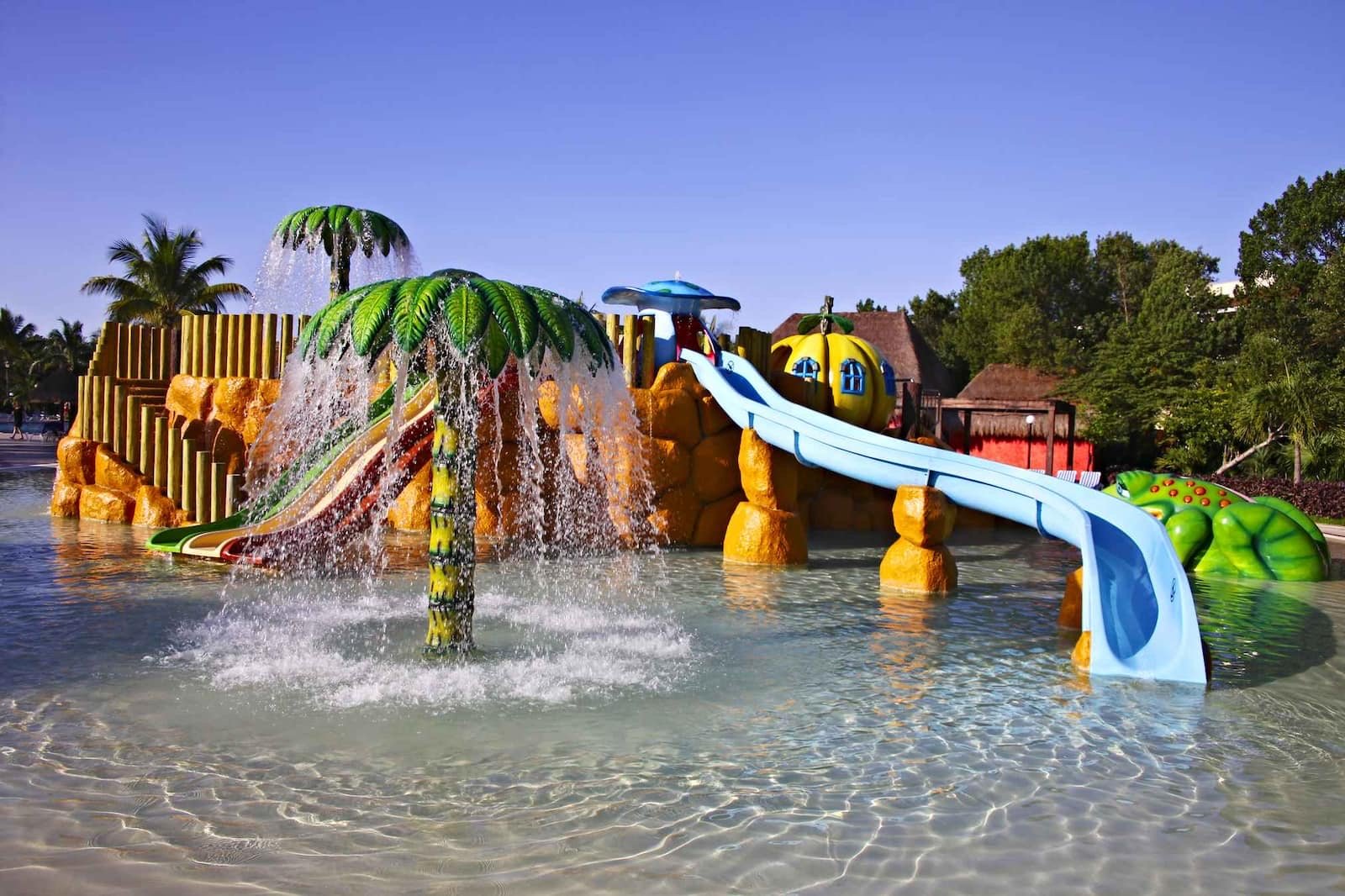 Parque acuático con toboganes de colores, palmeras de juguete y chorros de agua