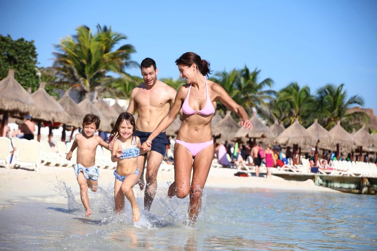 Una familia corre hacia el mar en una playa con palapas