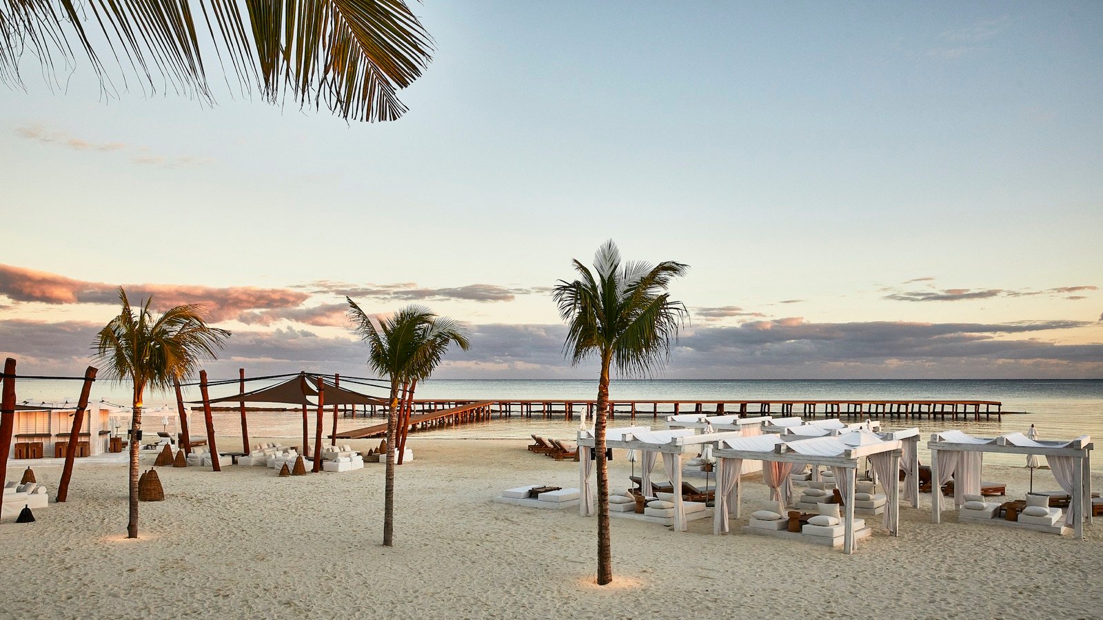 Atardecer en la playa con mesas y palmeras