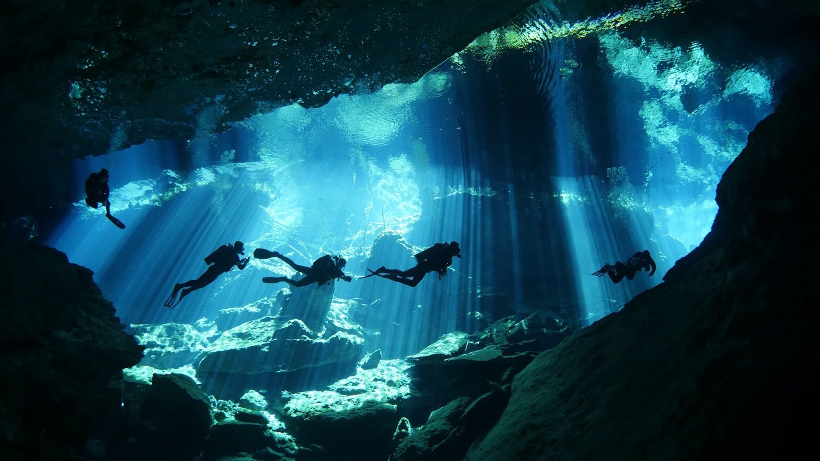 Buzos en un cenote con rayos de luz que entran al agua azul