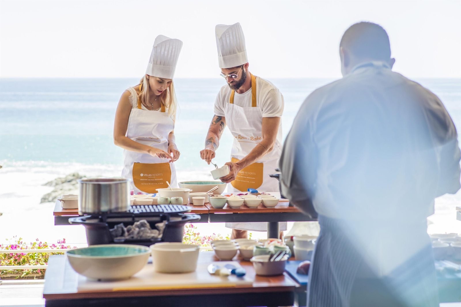 Dos chefs preparan comida en una terraza frente al mar