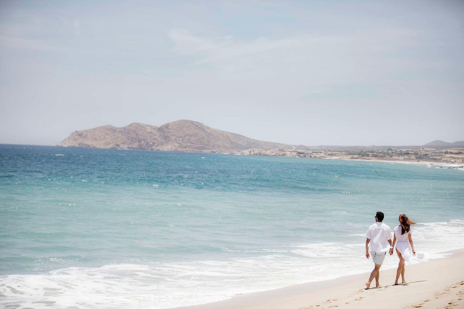 Una pareja camina por la orilla con las montañas al fondo