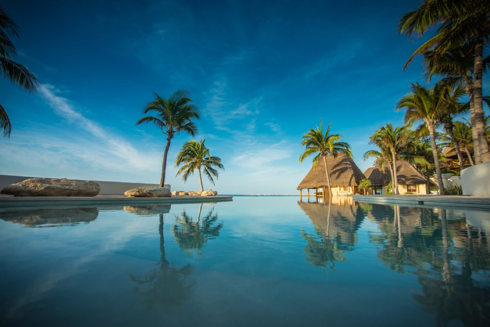 La alberca infinity de Mahekal con palmeras reflejadas en el agua