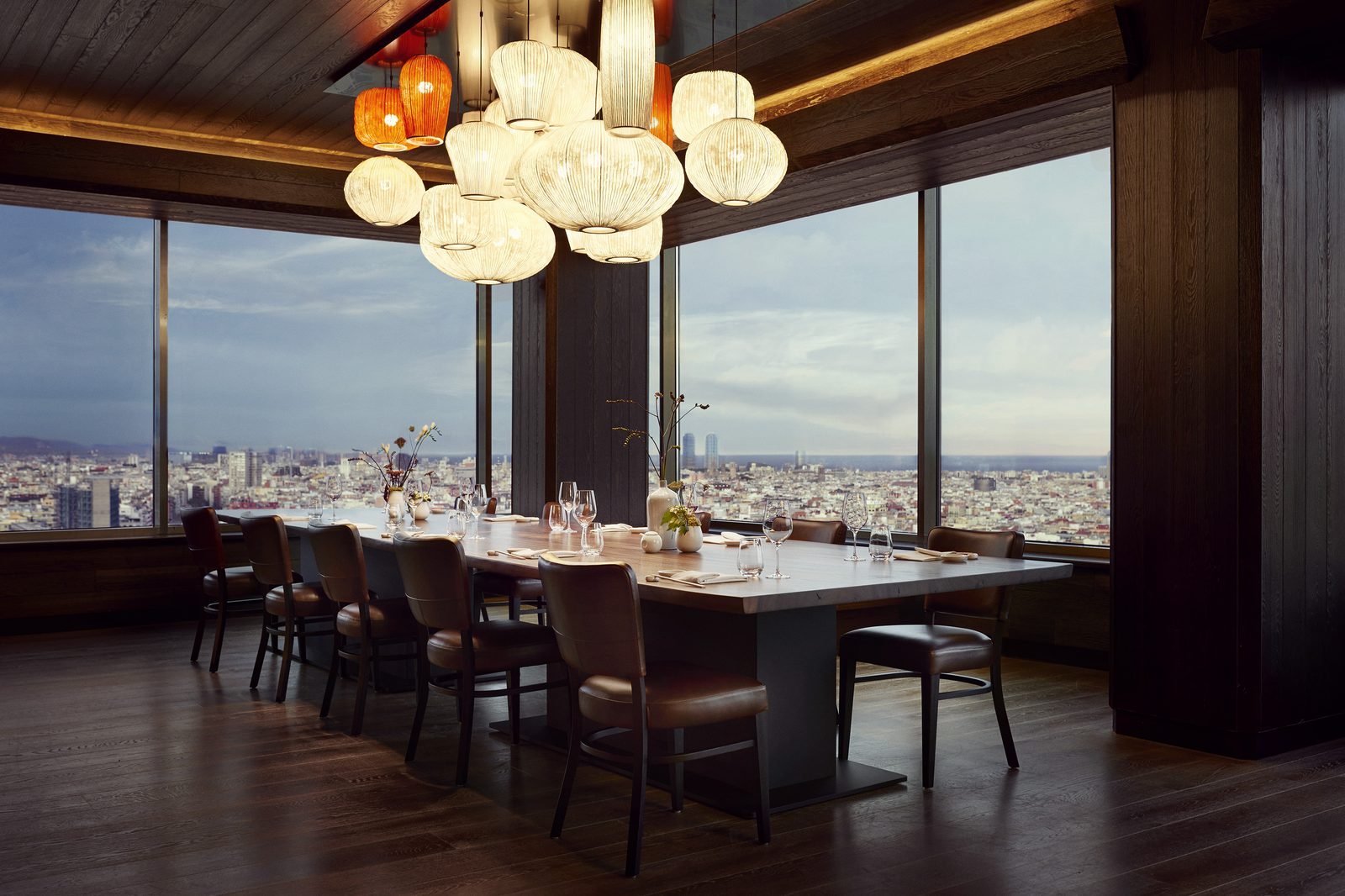 Comedor privado con una mesa larga y lámparas de papel frente a los ventanales