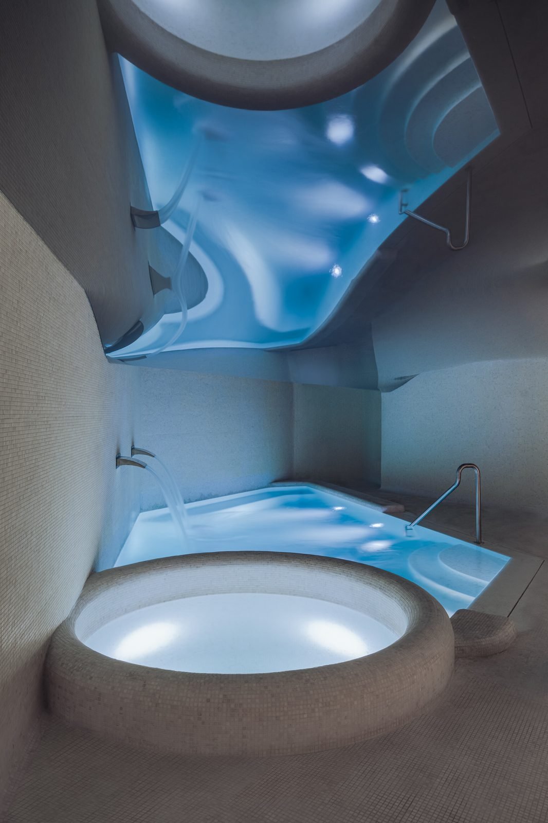 Una tina circular iluminada en tonos azules, en el circuito de aguas del spa