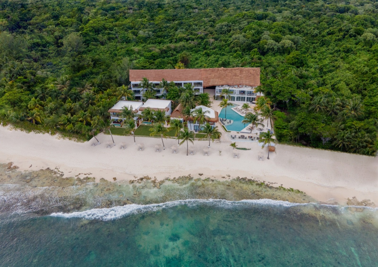 Vista aérea del hotel entre la selva y la playa de arena blanca, con el mar turquesa enfrente