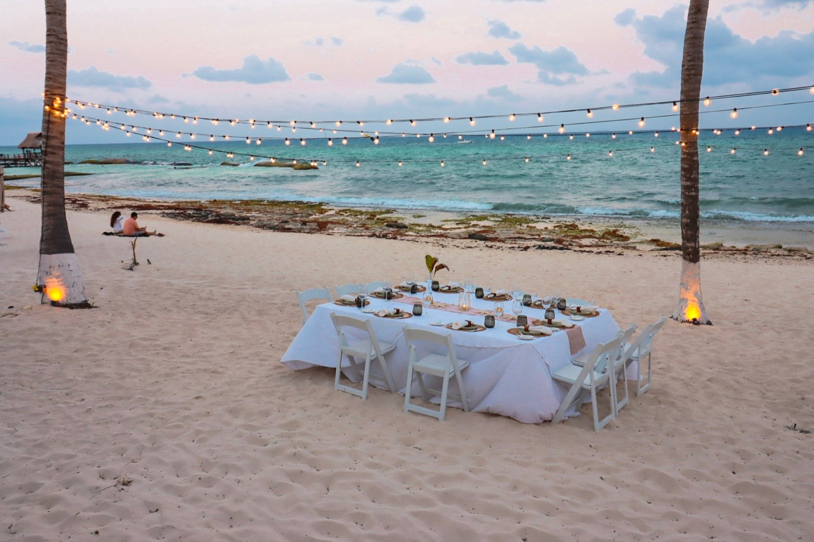 Mesa para cenar en la arena, bajo una línea de foquitos y frente al mar