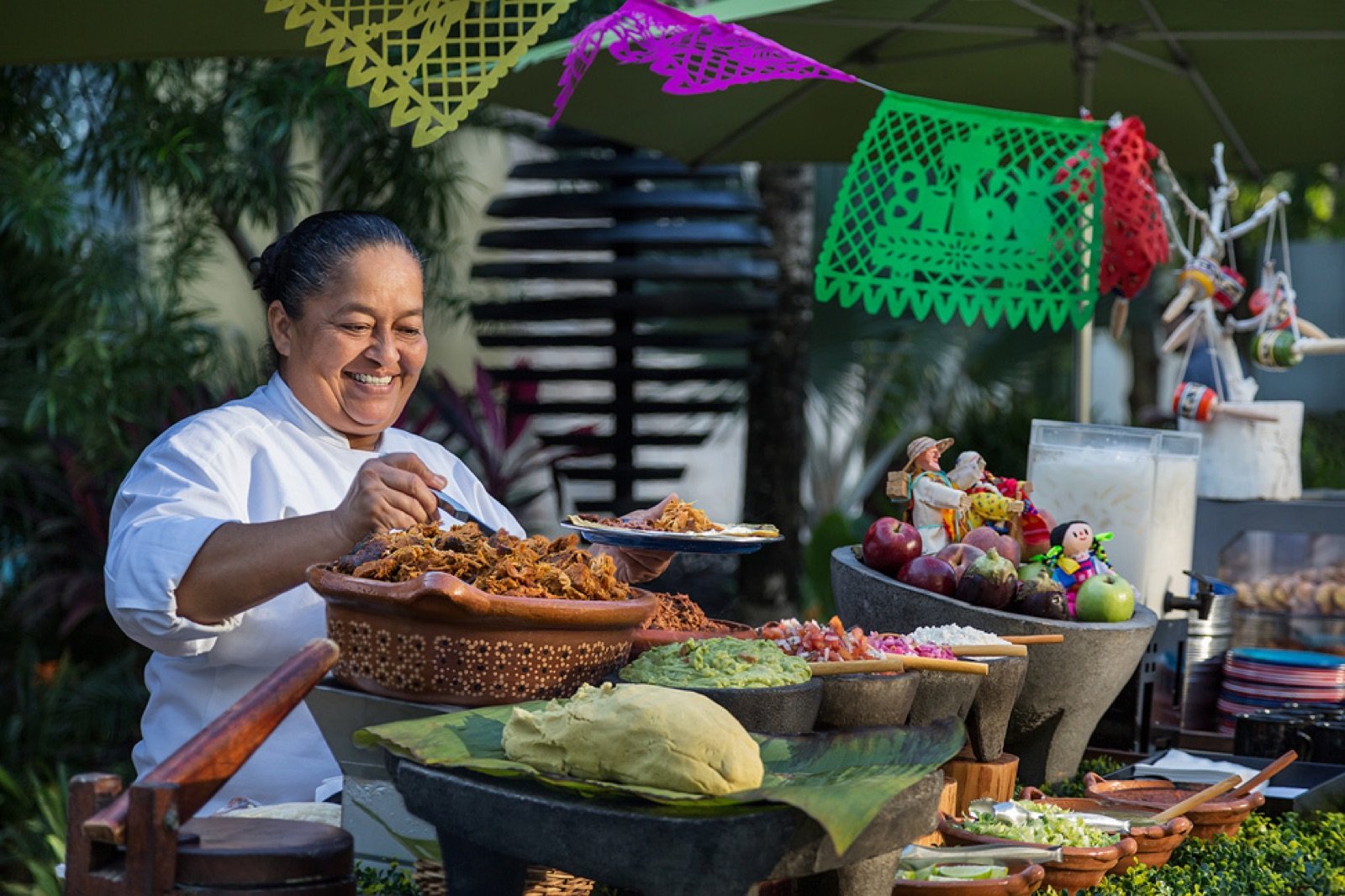 Una cocinera sonríe junto a canastas de chiles y verduras