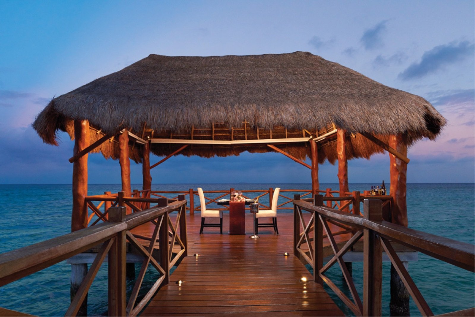 Mesa para cenar bajo una palapa al final de un muelle sobre el mar