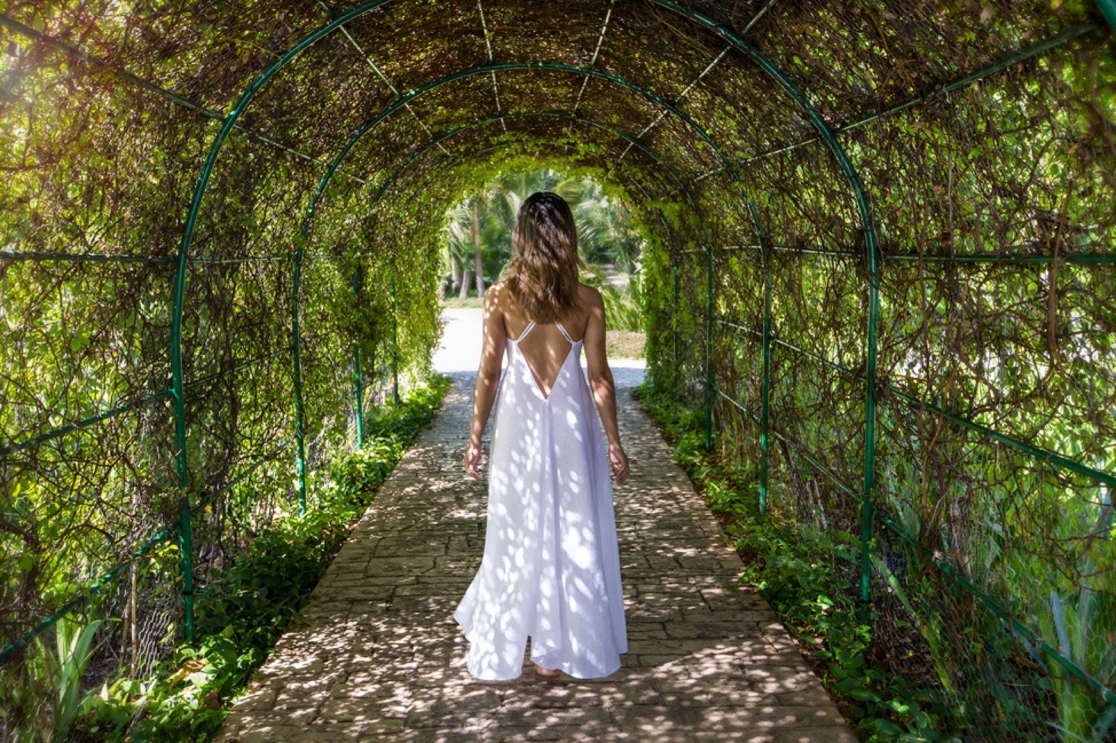 Una mujer de vestido blanco camina por un túnel de vegetación