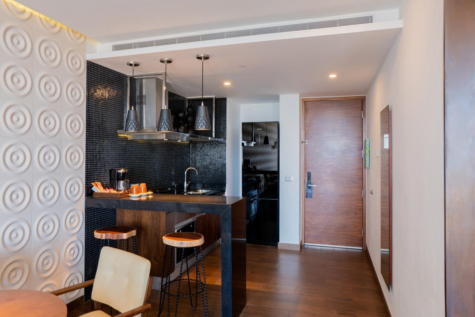 Cocina de una suite con barra de piedra negra, bancos altos y comedor