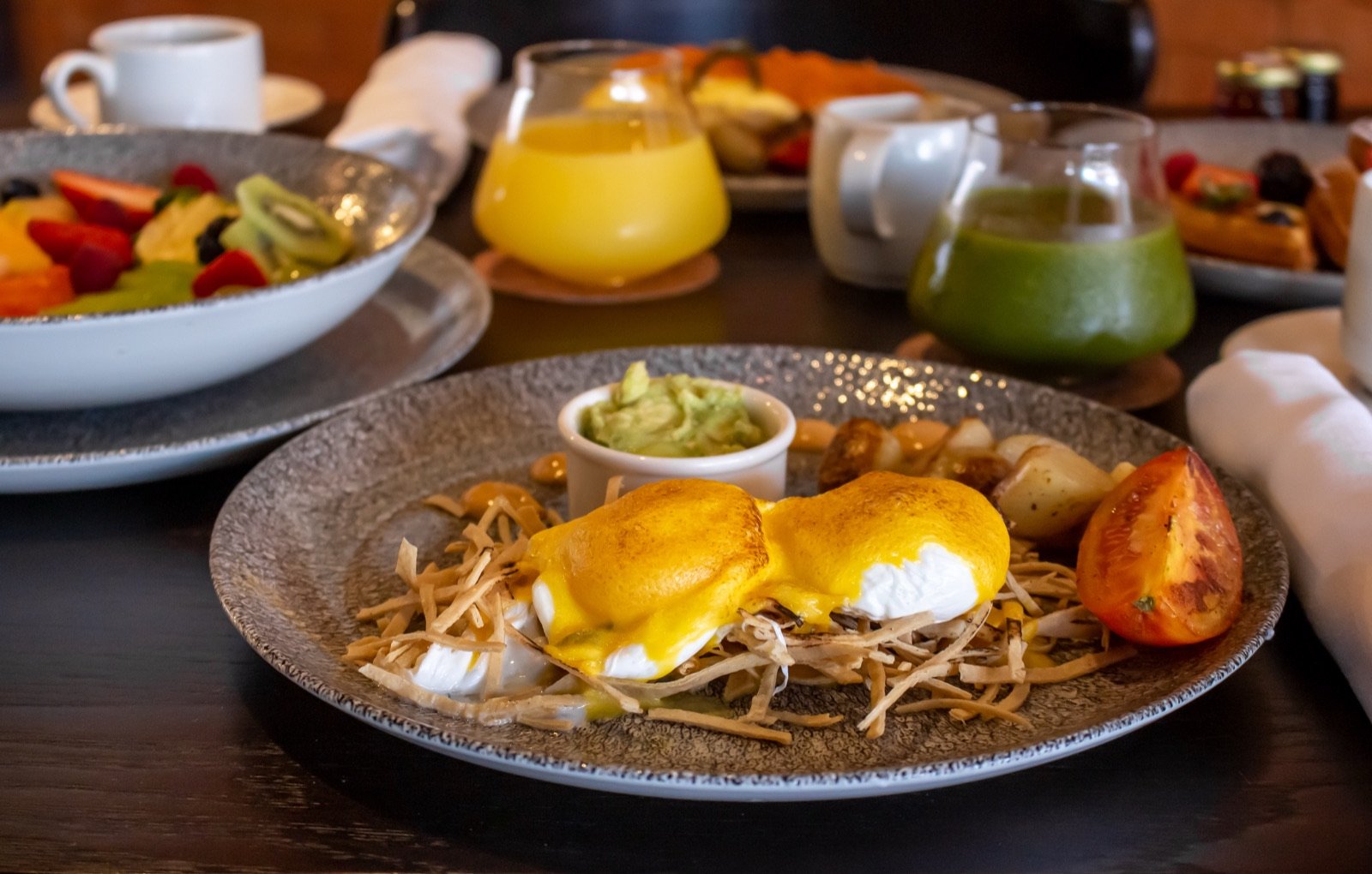 Huevos benedictinos, jugo de naranja y fruta en una mesa de Mercatto