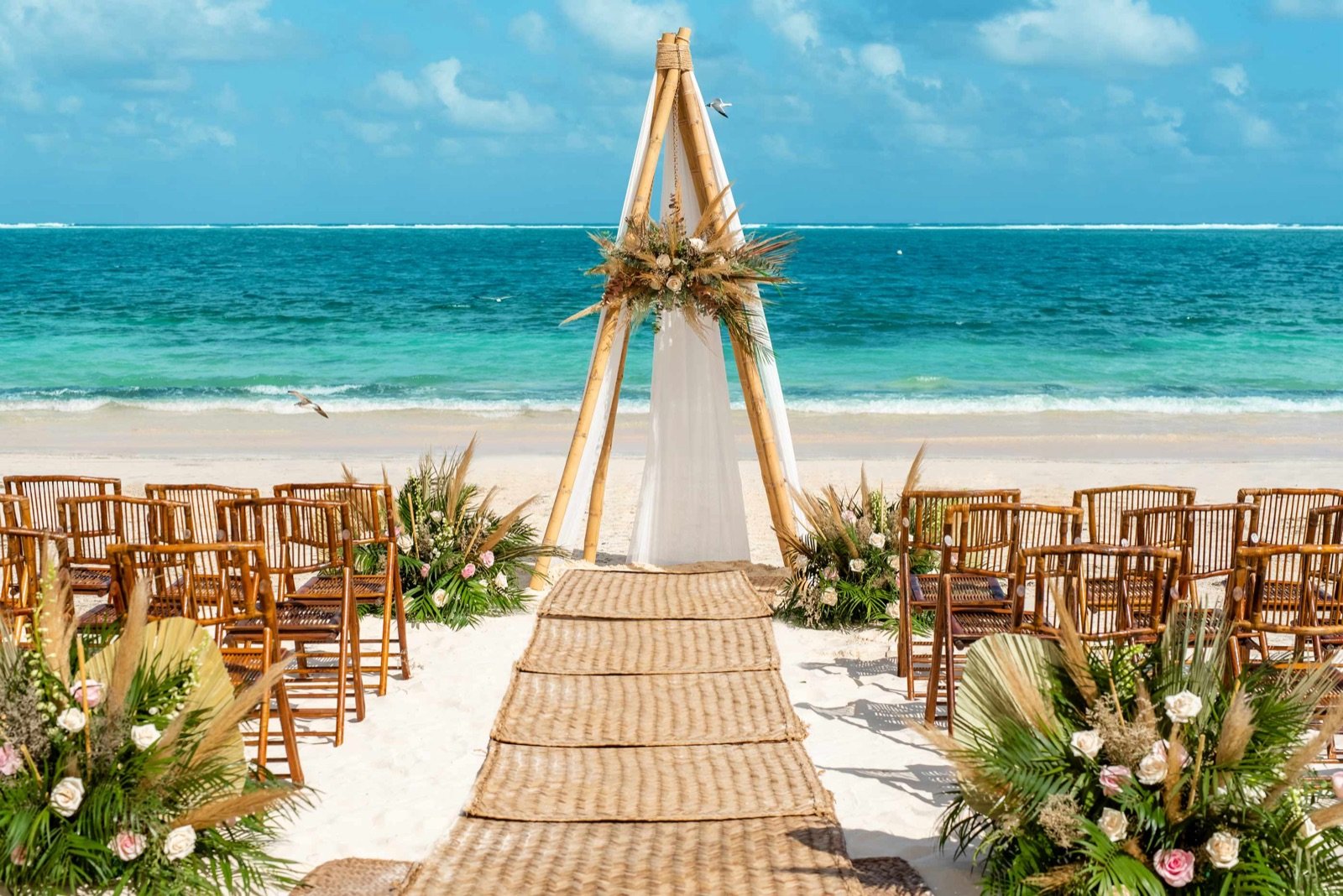 Montaje de boda en la playa con arco de madera y flores frente al mar