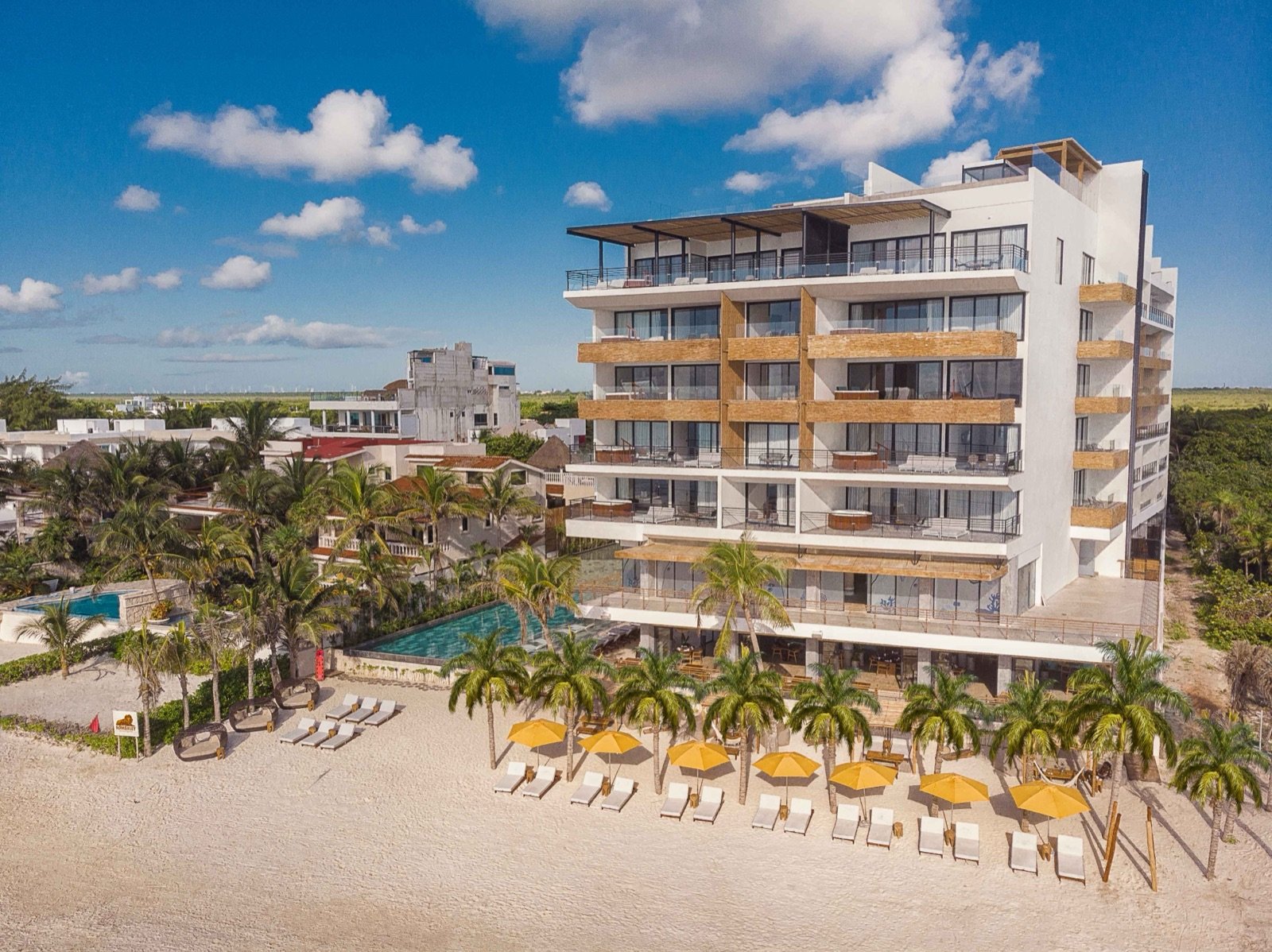 El hotel visto desde la playa, con sombrillas amarillas y palmeras