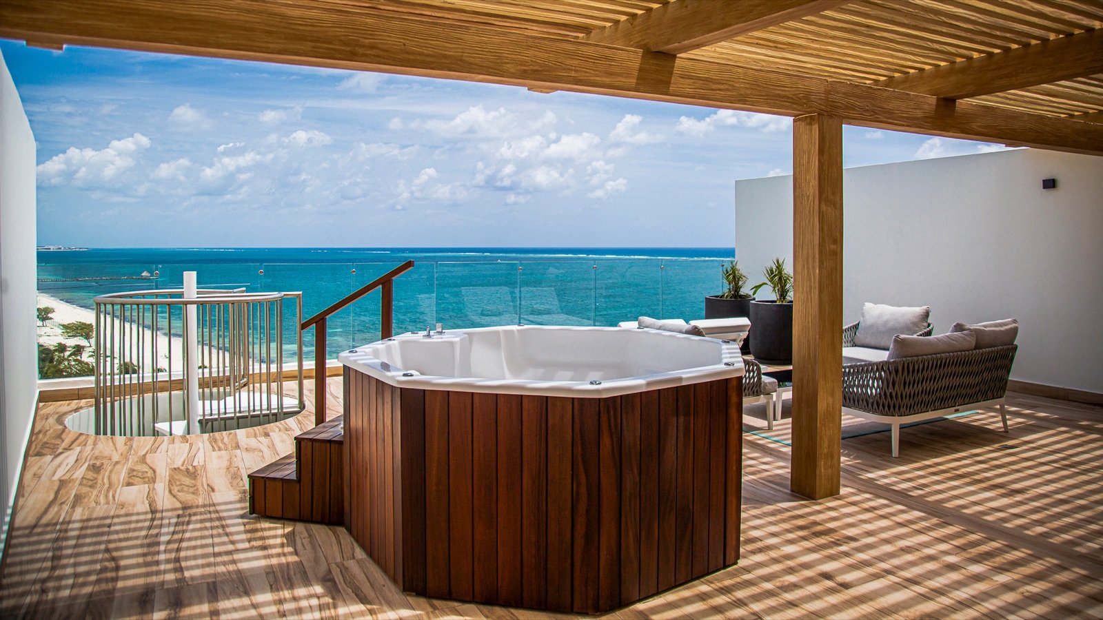 Azotea privada de un penthouse con jacuzzi de madera bajo una pérgola y el mar al fondo