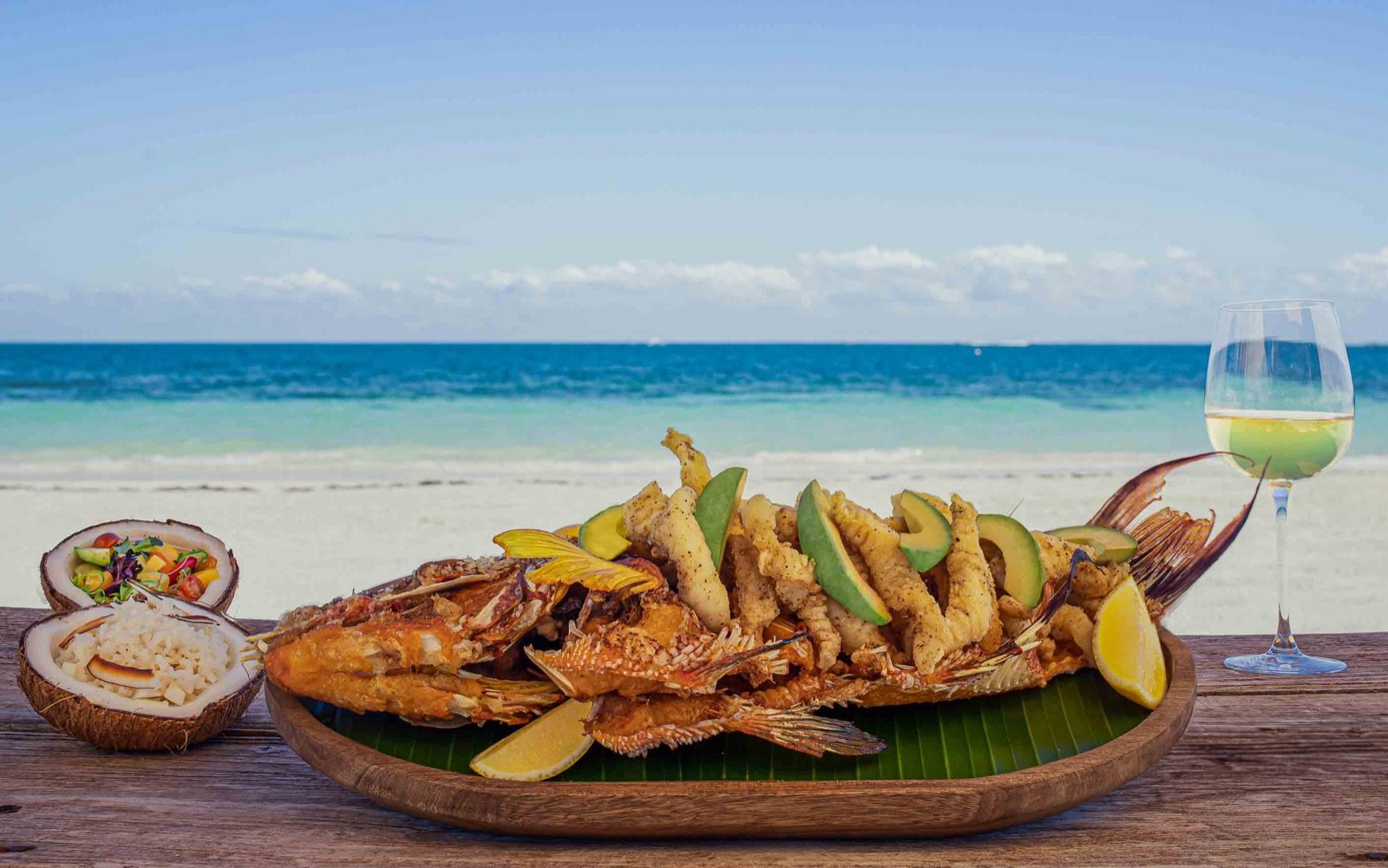 Pescado frito con verduras sobre una charola de madera frente al mar