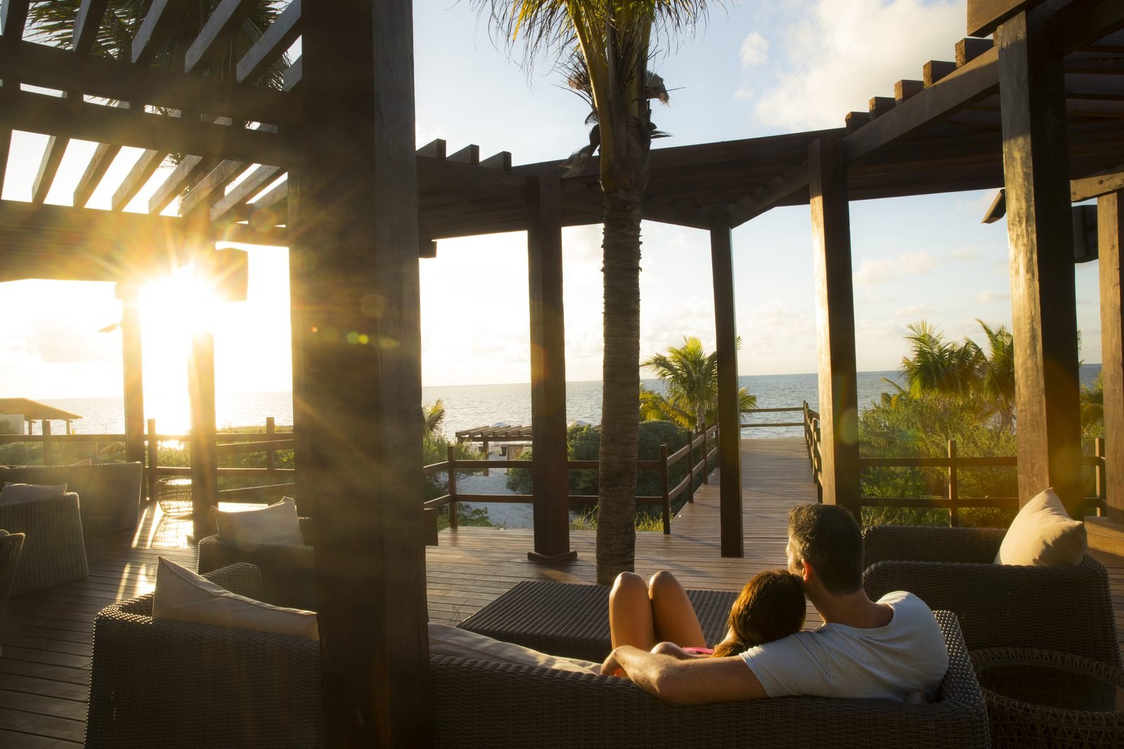 Una pareja descansa en una cama de playa bajo una pérgola al atardecer