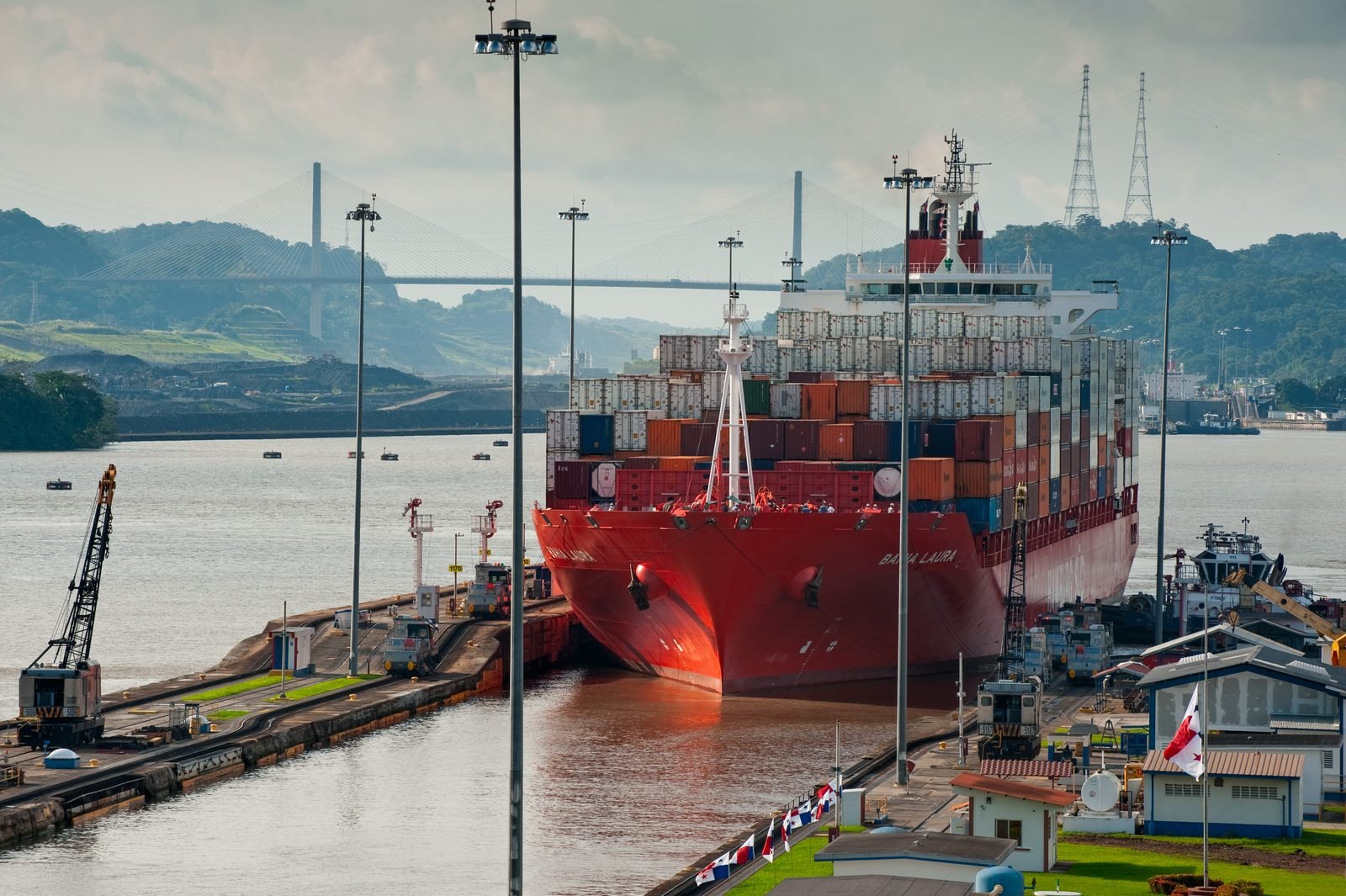 Un barco de carga rojo dentro de las esclusas de Miraflores, con los cerros verdes al fondo