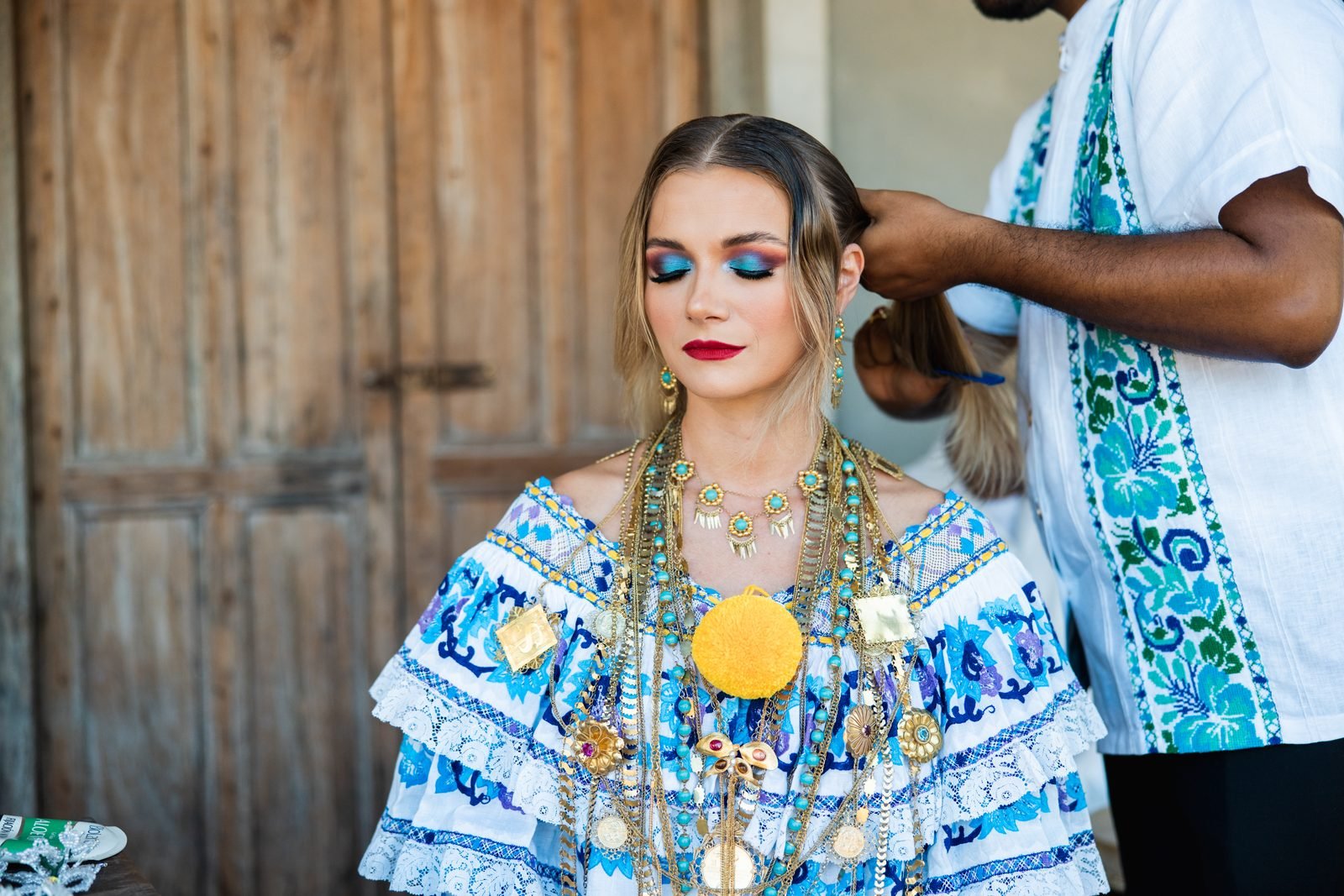 Una mujer con pollera de gala azul y blanca y tocados dorados, junto a músicos en Las Tablas